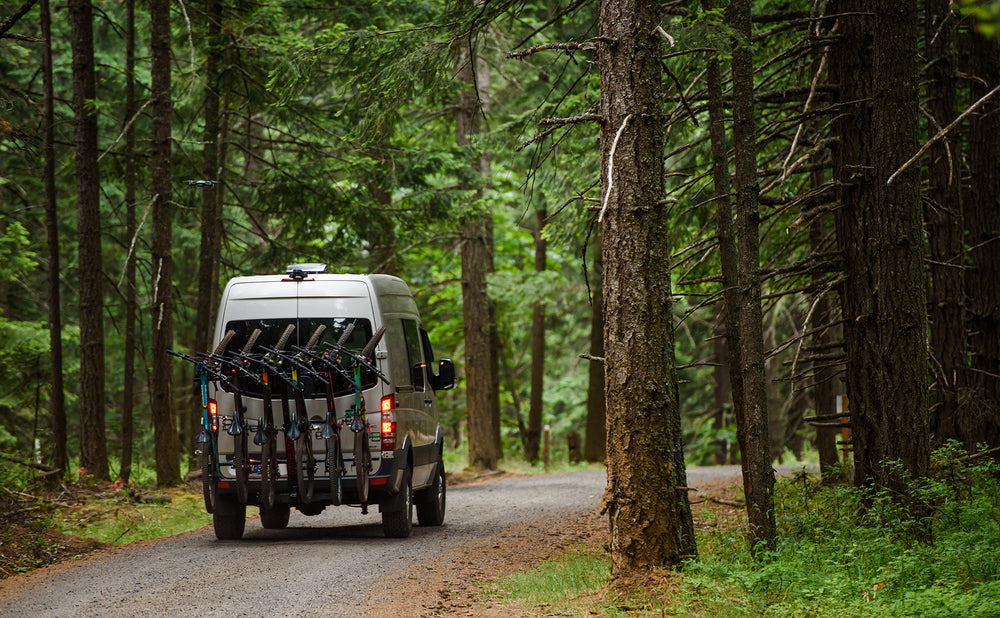 Rear of a van carrying a full rack of bikes in the forest